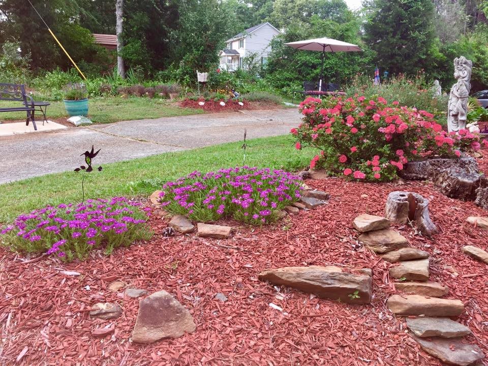 A landscaped garden with flowers, red mulch, and decorative stones.