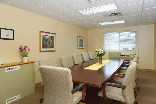 A well-lit conference room featuring a long wooden table surrounded by upholstered chairs and a floral centerpiece.