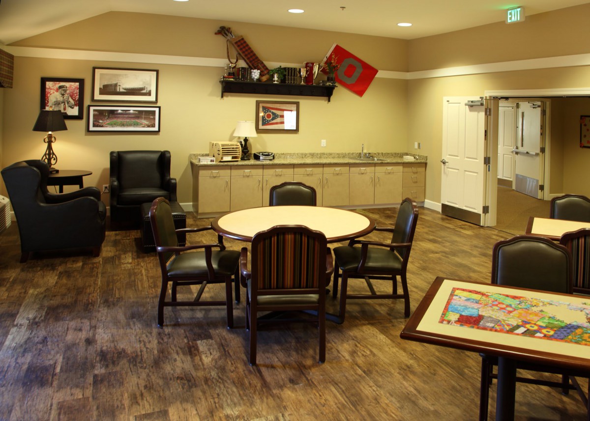 A cozy lounge area with a circular table and chairs, decorated with framed pictures and vintage items on the wall.