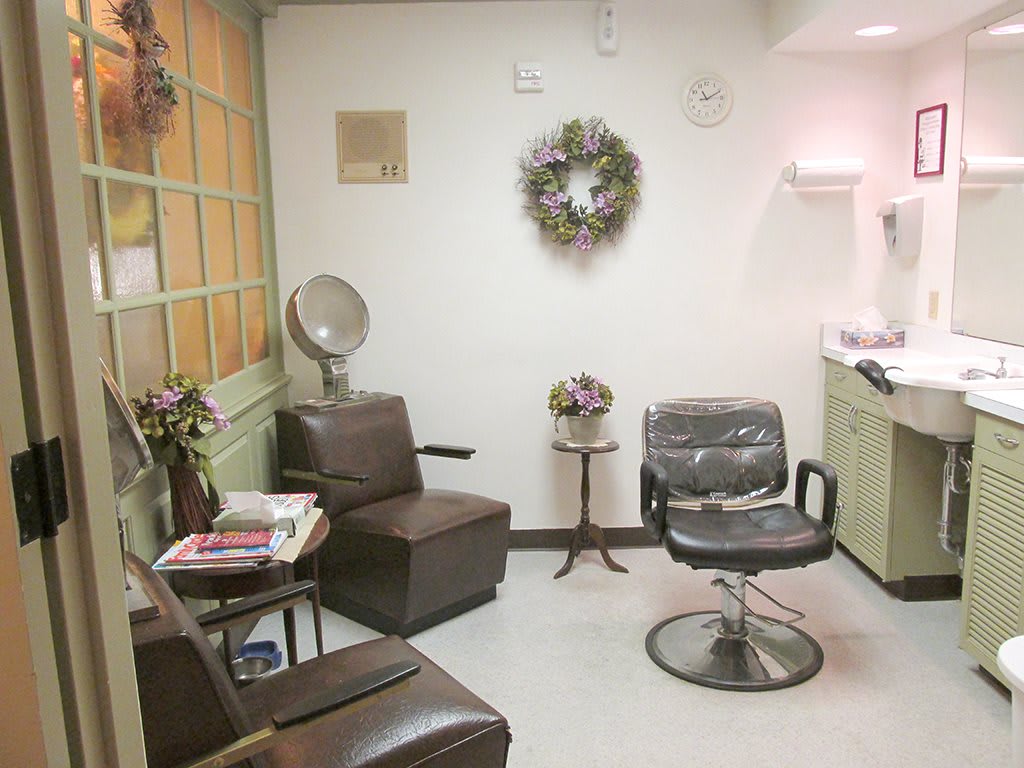 A cozy hair salon with comfortable seating, a styling chair, and decorative details such as a wreath and flowers.