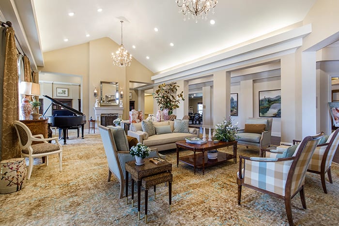 A spacious and elegantly designed living room featuring a grand piano, luxurious sofas, and chandeliers.