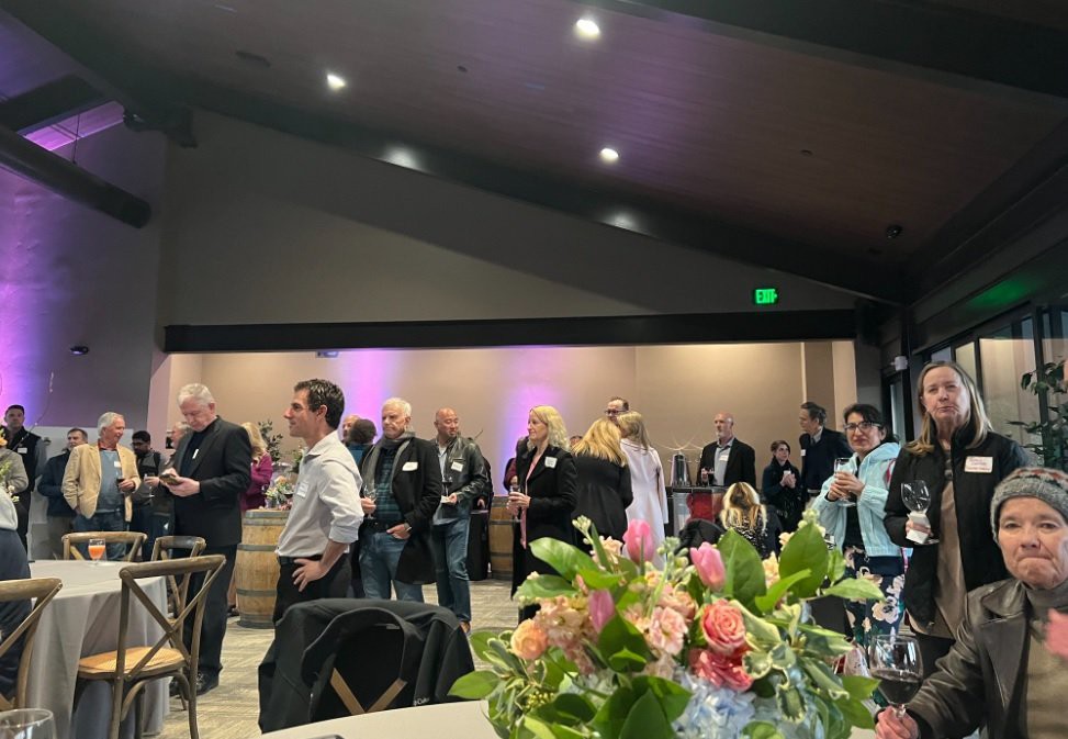 A social gathering with people mingling indoors, featuring a floral centerpiece.