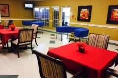 A dining area with tables covered in red cloth and striped chairs, featuring blue furniture and wall decorations.