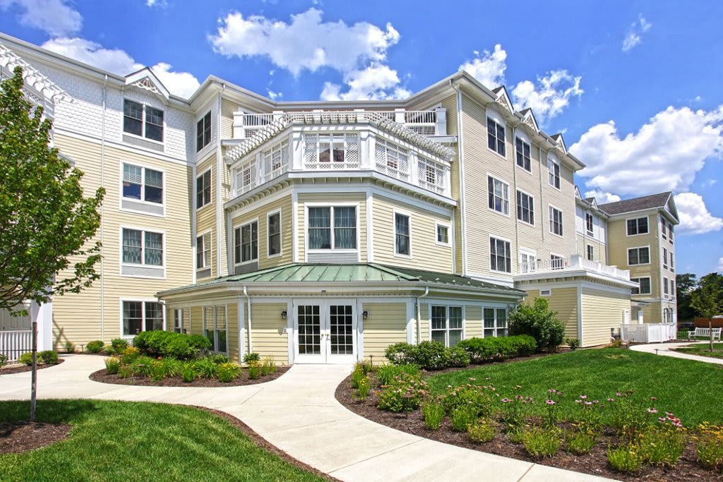 A modern residential building with well-maintained landscaping against a backdrop of a blue sky with clouds.