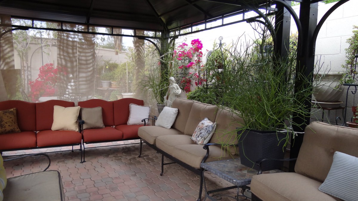 A cozy outdoor seating area under a gazebo, surrounded by lush plants and flowers.
