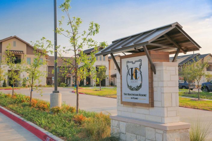 A suburban building complex with a landscaped entryway featuring a prominent sign.