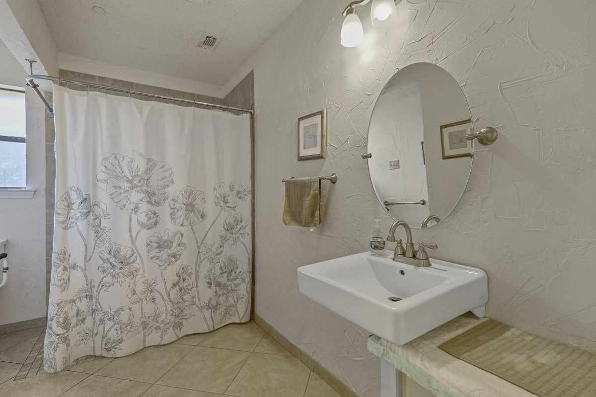 A modern bathroom with a pedestal sink, oval mirror, and floral shower curtain.