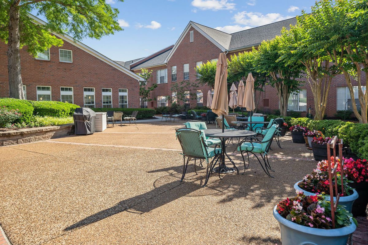 A sunny patio area with tables, chairs, and umbrellas set against a brick building.