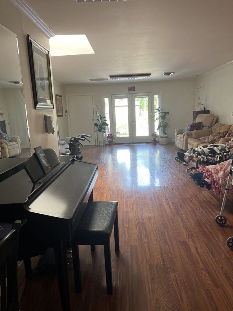 A spacious living room featuring a piano and hardwood flooring, with large glass doors allowing natural light to fill the space.