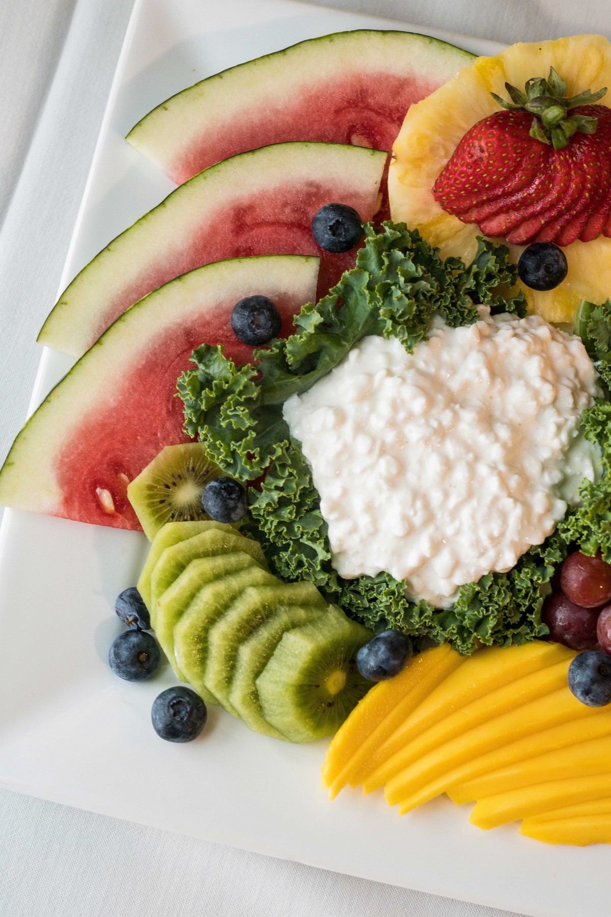 A vibrant and healthy plate featuring cottage cheese surrounded by a variety of fresh fruits including watermelon, kiwi, blueberries, strawberries, and mango.