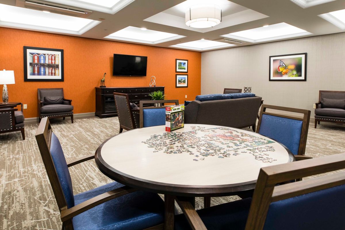 A cozy living room area with a round table and chairs, a television mounted on an orange accent wall, and comfortable seating.