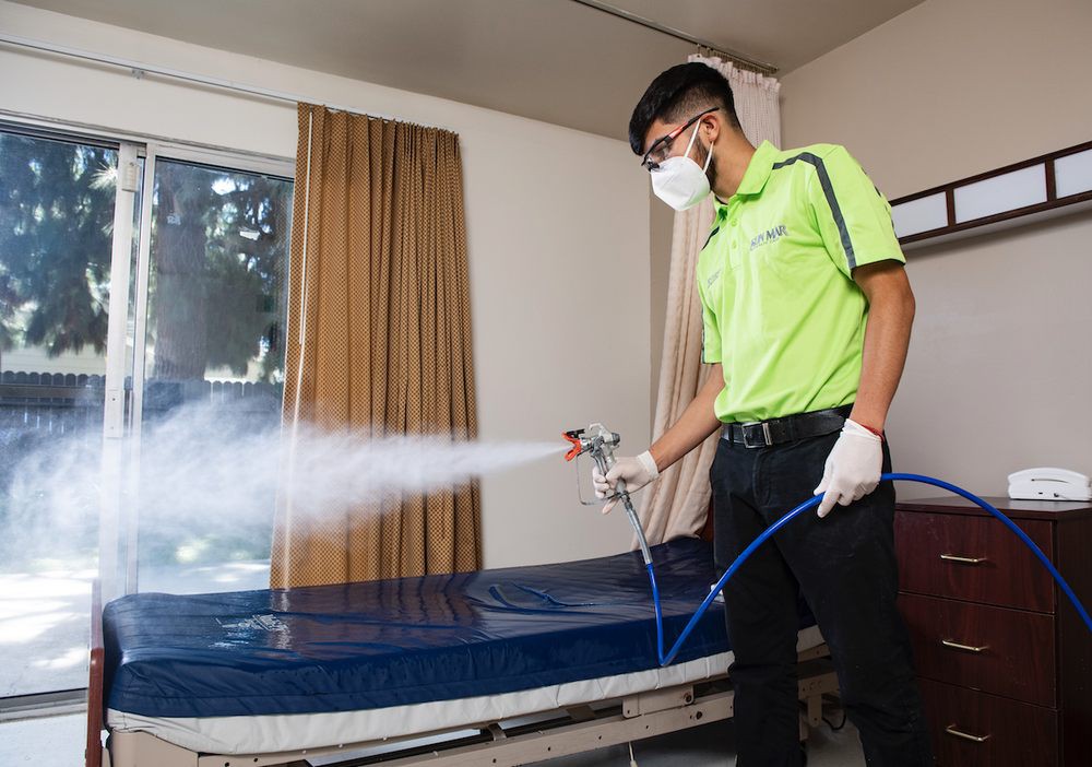 A person wearing protective gear is disinfecting a room using a spray device.