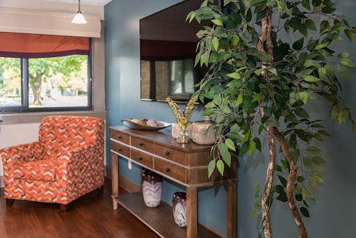 A cozy living space featuring a wooden console table, decorative items, a vibrant chair, and lush greenery.