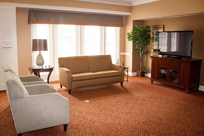 A cozy living room with warm tones, featuring a sofa, chairs, and a large window with curtains.