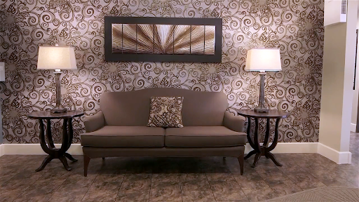A cozy living room setup featuring a stylish sofa, decorative pillow, elegant lamp, and patterned wallpaper.