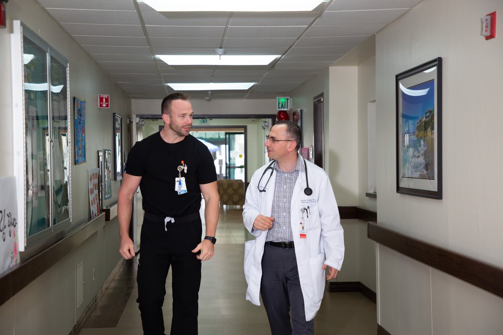 A doctor and a security officer walking and talking in a hospital corridor.