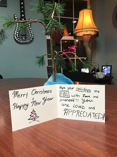 A handwritten holiday greeting card wishing 'Merry Christmas' and 'Happy New Year', displayed next to a small decorative tree.