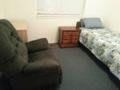 A simple bedroom with a bed, an armchair, and a nightstand.