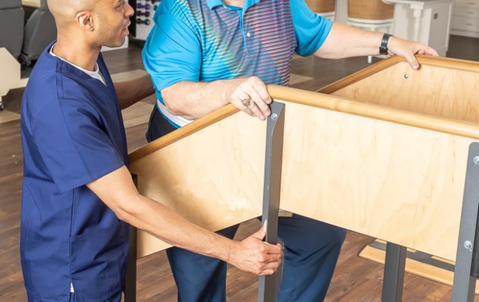 A healthcare professional assists a patient with physical therapy exercises using parallel bars.