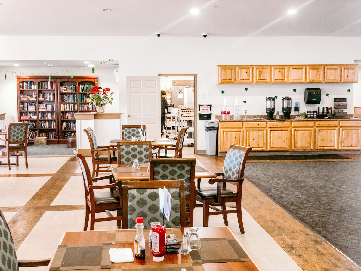 A cozy restaurant interior with neatly arranged tables and chairs, featuring a view of the kitchen area.