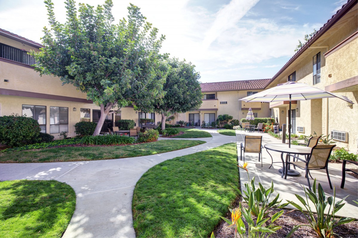 A well-maintained residential courtyard featuring lush greenery, trees, and outdoor seating areas.