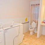 An accessible bathroom featuring a walk-in bathtub, toilet, sink, and supportive grab bars.