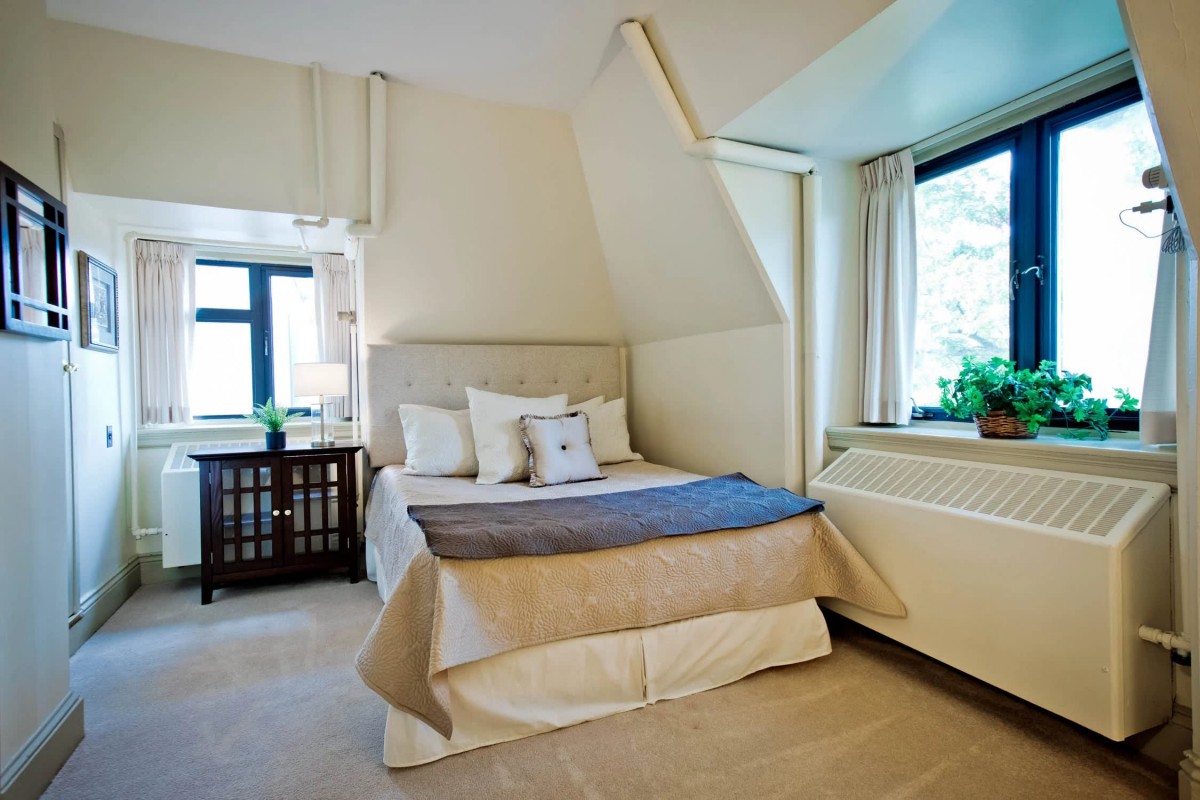 A cozy bedroom with a neatly made bed, accented by soft lighting and a view of greenery through the window.