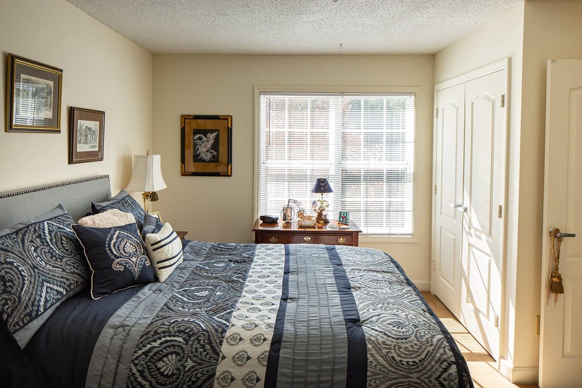 A cozy bedroom with a neatly made bed, patterned bedding, and natural light filtering through the window.