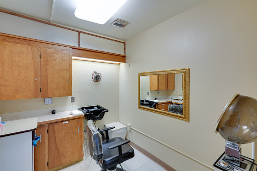 A well-lit hair salon room featuring a mirror, chair, and wooden cabinetry.