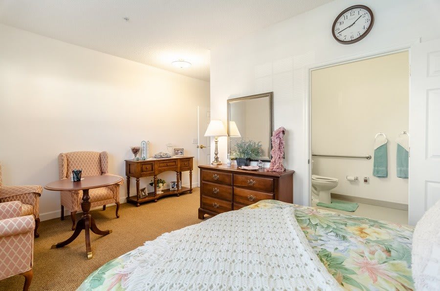 A cozy bedroom with classic furniture and decor, featuring a bed, dresser, chairs, and a lamp.