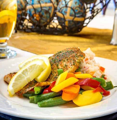 A gourmet dish featuring seasoned salmon with a side of colorful vegetables and lemon slices.