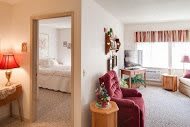 A cozy apartment interior featuring a living room with a red chair and television, alongside a view into the adjacent bedroom.