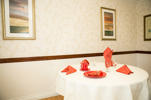 A beautifully set dining table with red accents against a cream-colored wall, featuring decorative artwork.