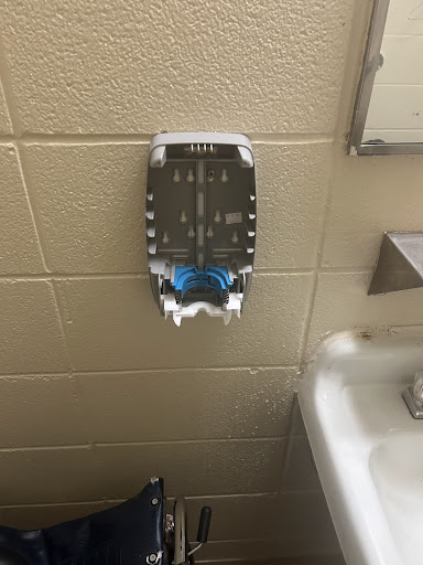 A wall-mounted soap dispenser in a bathroom, featuring blue accents.