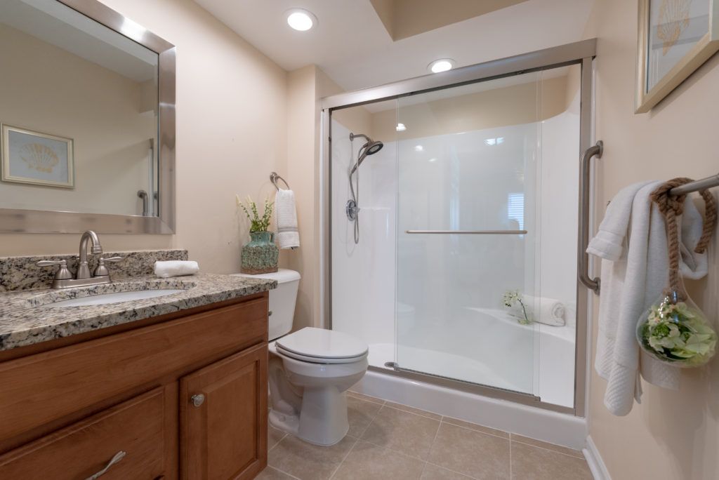 A modern bathroom featuring a glass-enclosed shower, toilet, and sink with a wooden cabinet.