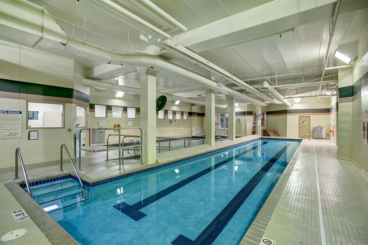 An indoor lap pool with clear blue water, surrounded by tiled flooring and white walls.