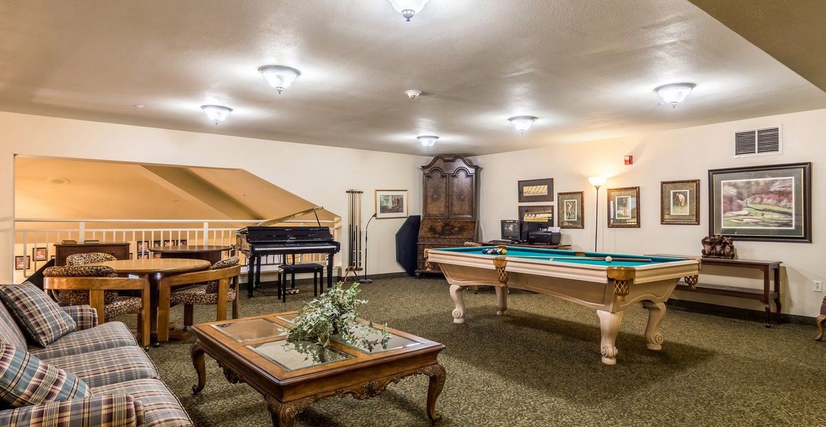 A cozy game room featuring a pool table, piano, and elegant furniture with framed artwork on the walls.