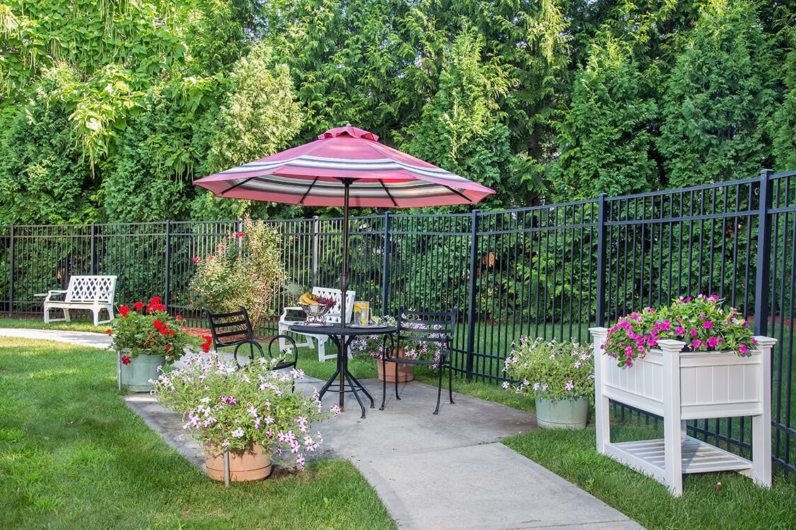 A cozy garden patio with a striped umbrella, surrounded by lush greenery and colorful flowers.