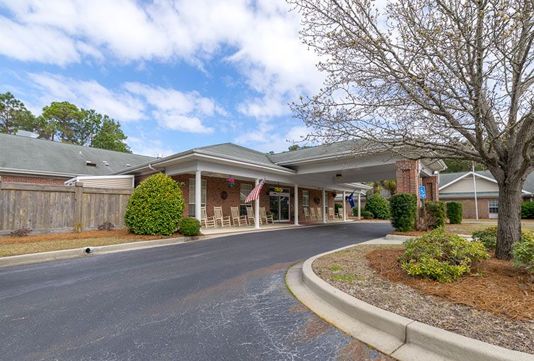 A building with a covered driveway, surrounded by trees and landscaping under a cloudy sky.