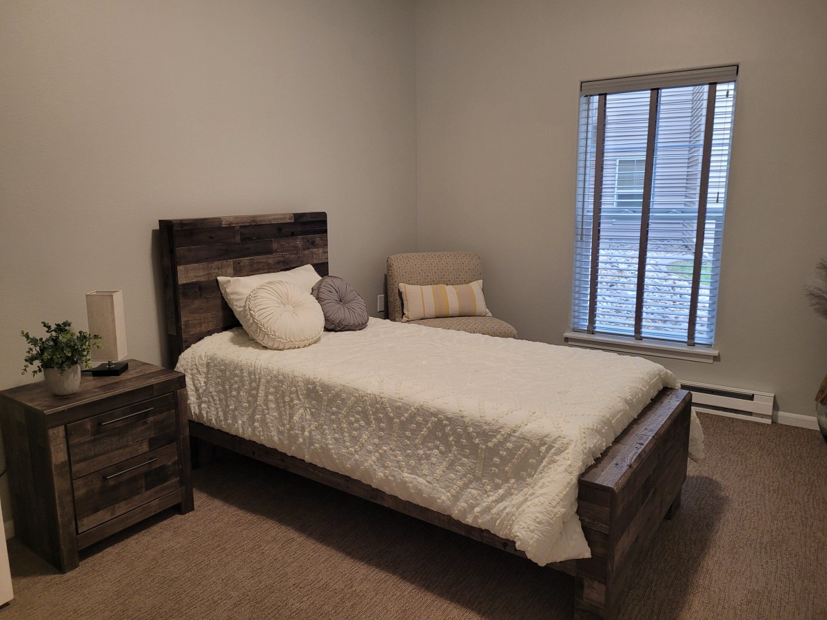 A minimalist bedroom with a single bed, nightstand, and a window.