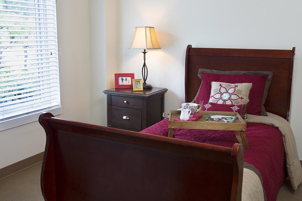 A cozy bedroom with a wooden bed, nightstand, and lamp, featuring a tray on the bed.