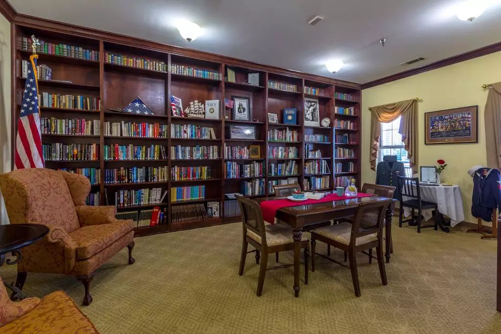 A cozy library with wooden bookshelves filled with books, featuring a reading table and chairs.
