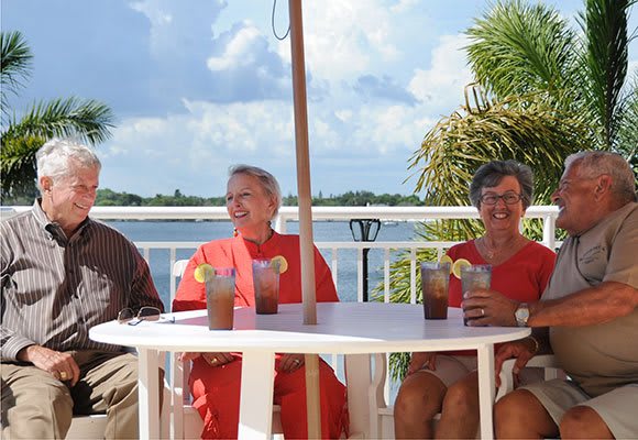 A group of people sitting at a table by the water, enjoying drinks on a sunny day.