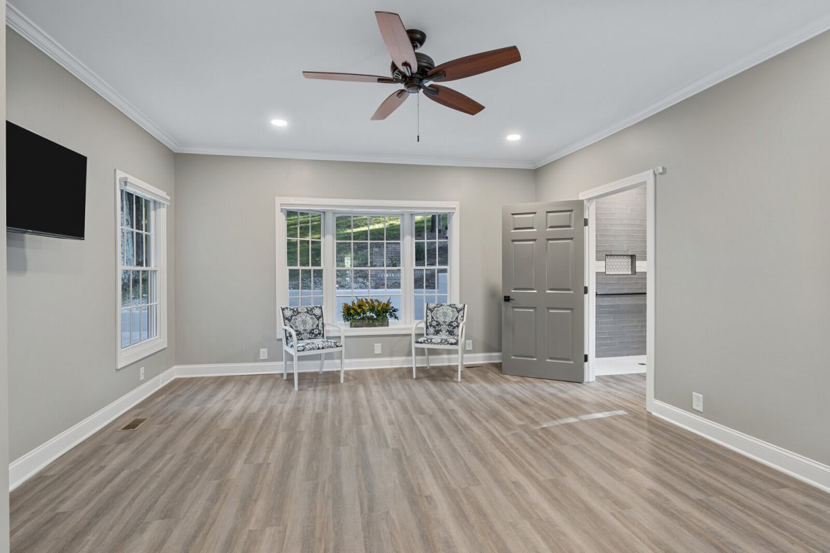 A modern living room with wood flooring, a ceiling fan, and large windows.