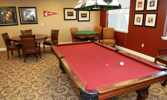 A cozy recreation room featuring a red pool table, comfortable chairs, and a card table.