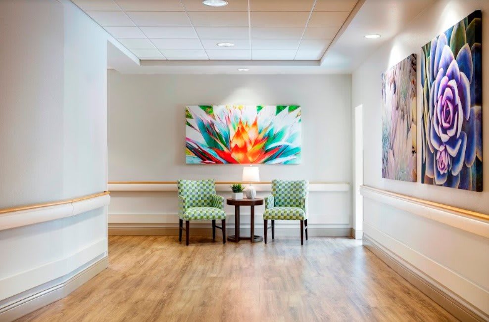 A bright and inviting hallway features two green chairs and a small table, highlighted by a colorful abstract painting on the wall.