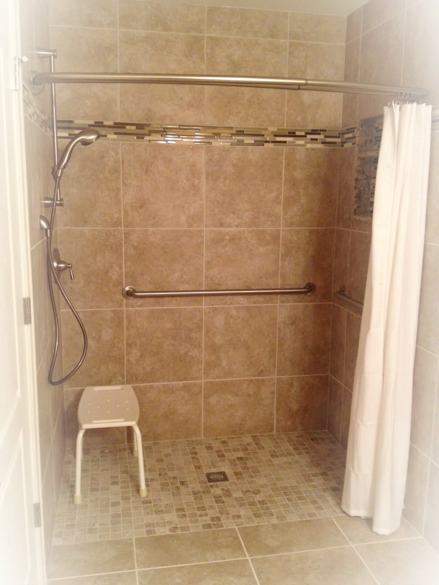 An accessible bathroom shower with a grab bar, curtain, and shower chair.