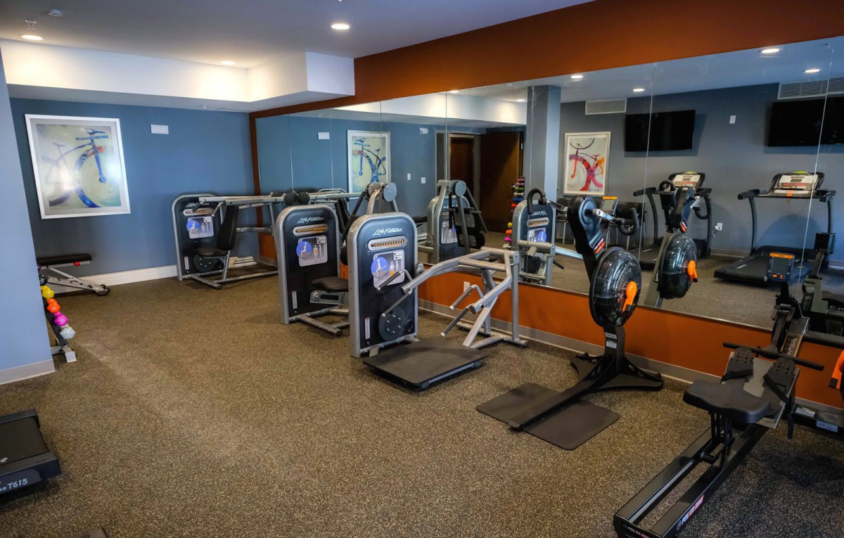 A fitness center with various exercise machines and mirrored walls.