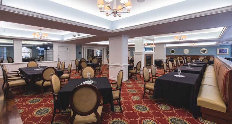 An elegant conference room setup with round tables and upholstered chairs, featuring a patterned carpet and modern chandeliers.