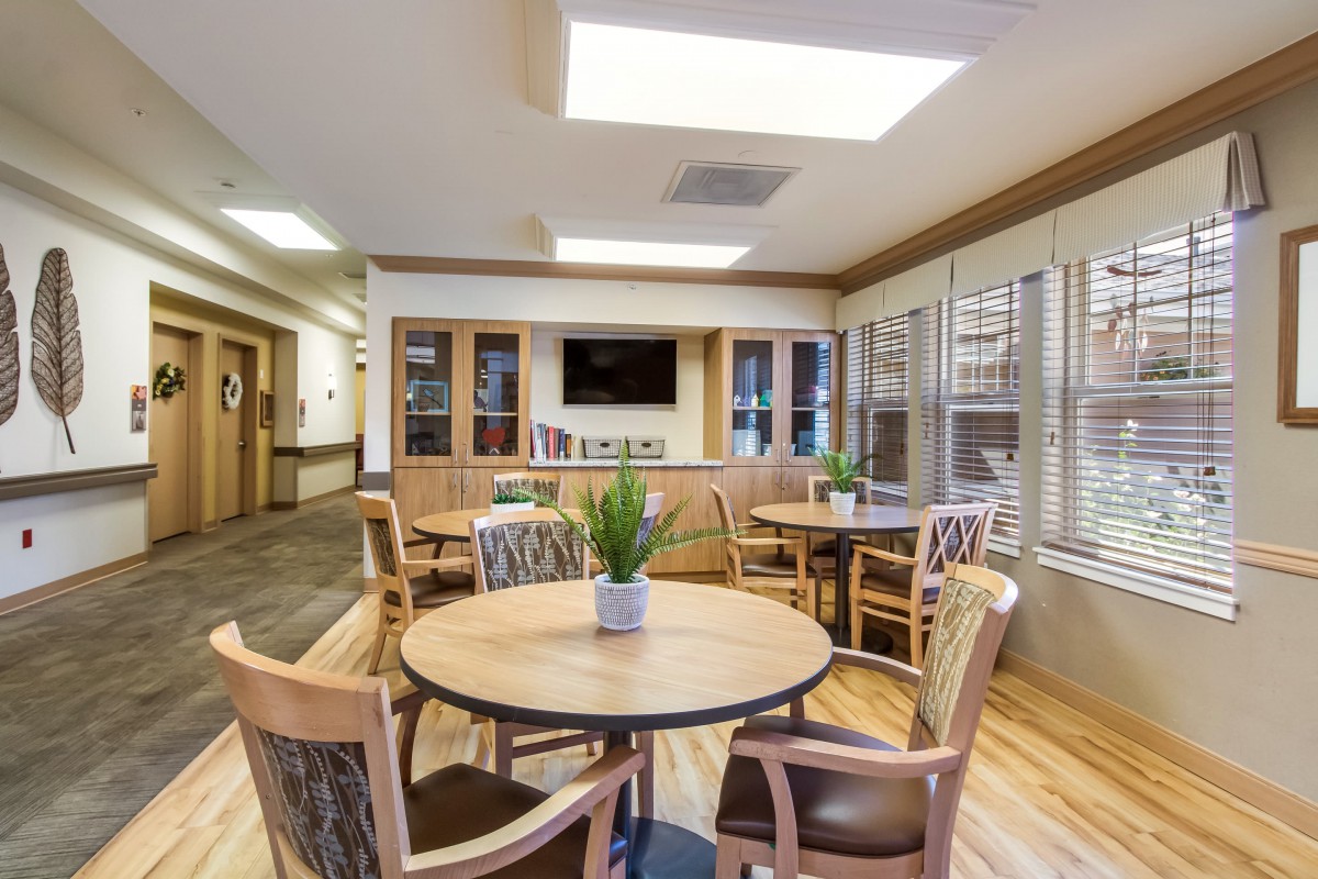 A cozy community seating area with tables and chairs, featuring a television and decorative plants.